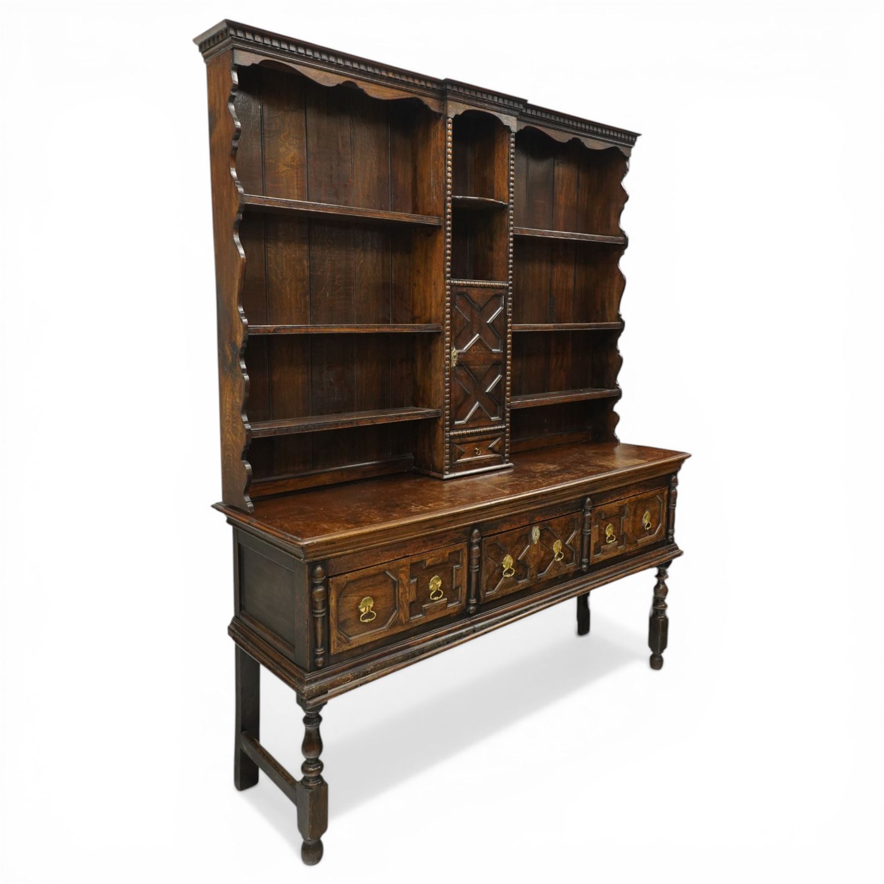 19th century Jacobean Revival oak dresser and rack, the upper section with open shelves and central cupboard, flanked by bobbin moulded uprights, the base fitted with three carved drawers with brass ring handles, raised on turned supports united by stretchers