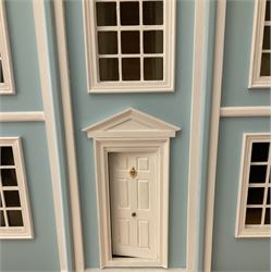 Georgian style wooden double fronted three-storey dolls house with pale blue stucco finish under a faux tiled roof with two chimney stacks, the double hinged front opening to reveal six fully decorated rooms with floor coverings, central staircase, porcelain fitted bathroom, kitchen with deep white sink and Aga cooker, electric lighting with adaptor, fully furnished with French style and other furniture, grand piano etc, and comprehensive range of accessories H82cm W61cm D31cm