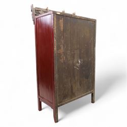 Early 20th century Chinese lacquered marriage cabinet, of rectangular form in red lacquer, fitted with double doors centred by circular brass lock plate and drop handles, the interior with shelves and two short drawers, cornice and apron with giltwood foliate and figural carving, together with an elaborately pierced and gilded wooden cresting panel carved with scenes of figures within pavilions and stylised dragons