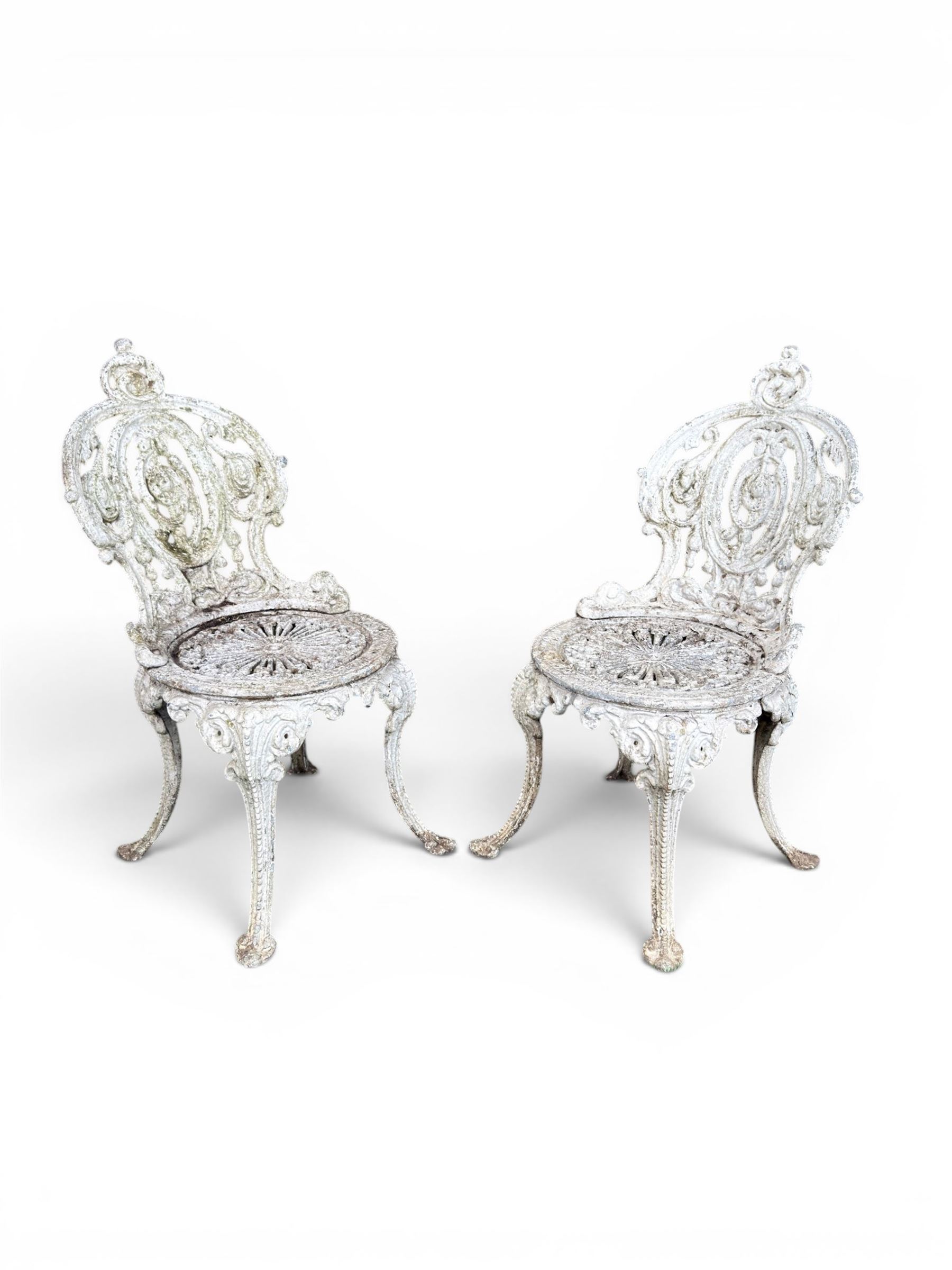 Pair of white painted cast metal garden chairs, ornate reclined backs, circular pierced seats on cabriole legs