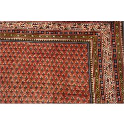 West Persian Boteh-Mir hand-knotted rug, madder red field densely decorated with a repeating lattice of of small boteh motifs arranged in diagonal rows enclosed by a broad border of stylized geometric devices and angular floral ornament between multiple guard stripes with cotton fringe ends