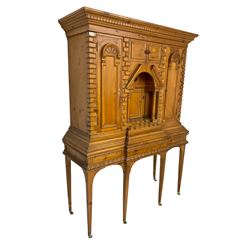 20th century pine architectural collector's cabinet on stand, projecting dentil cornice over various compartments, central recessed arch with turned pillar supports and sloped arch pediment, fitted with four cupboards, false brickwork uprights to front and corners, central hidden drawer revealing cube work surface, lower moulded plinth, the stand with foliate carved mouldings, on six square tapering supports with brass castors