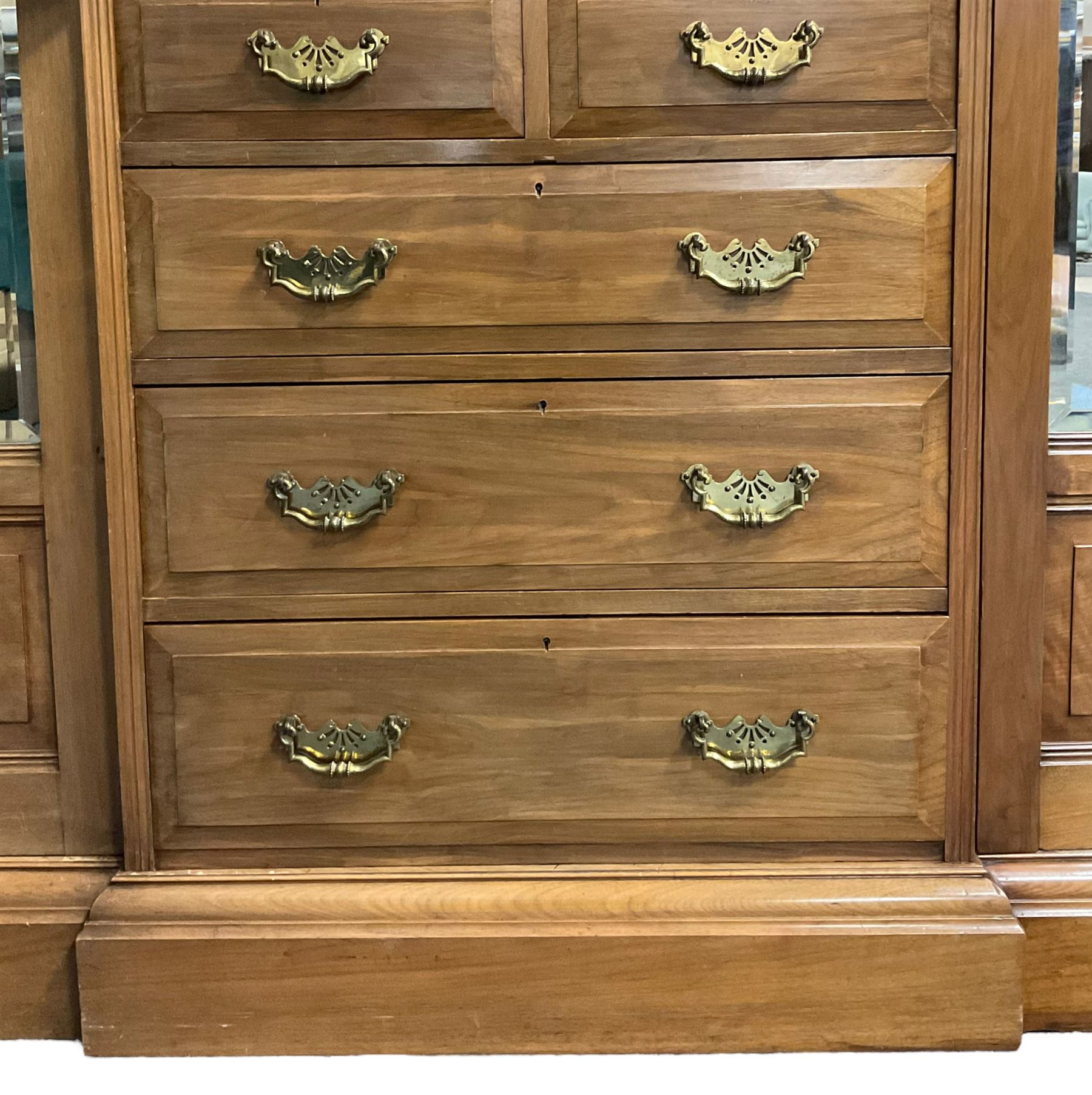 Edwardian walnut combination breakfront triple wardrobe, projecting cornice over cushioned and fluted frieze, central fielded panelled cupboard carved with foliate decoration above two short and three long drawers, flanked by two bevelled mirror doors enclosing hanging hooks with single drawers to base, retailed by J Tonks & Sons, Scarborough