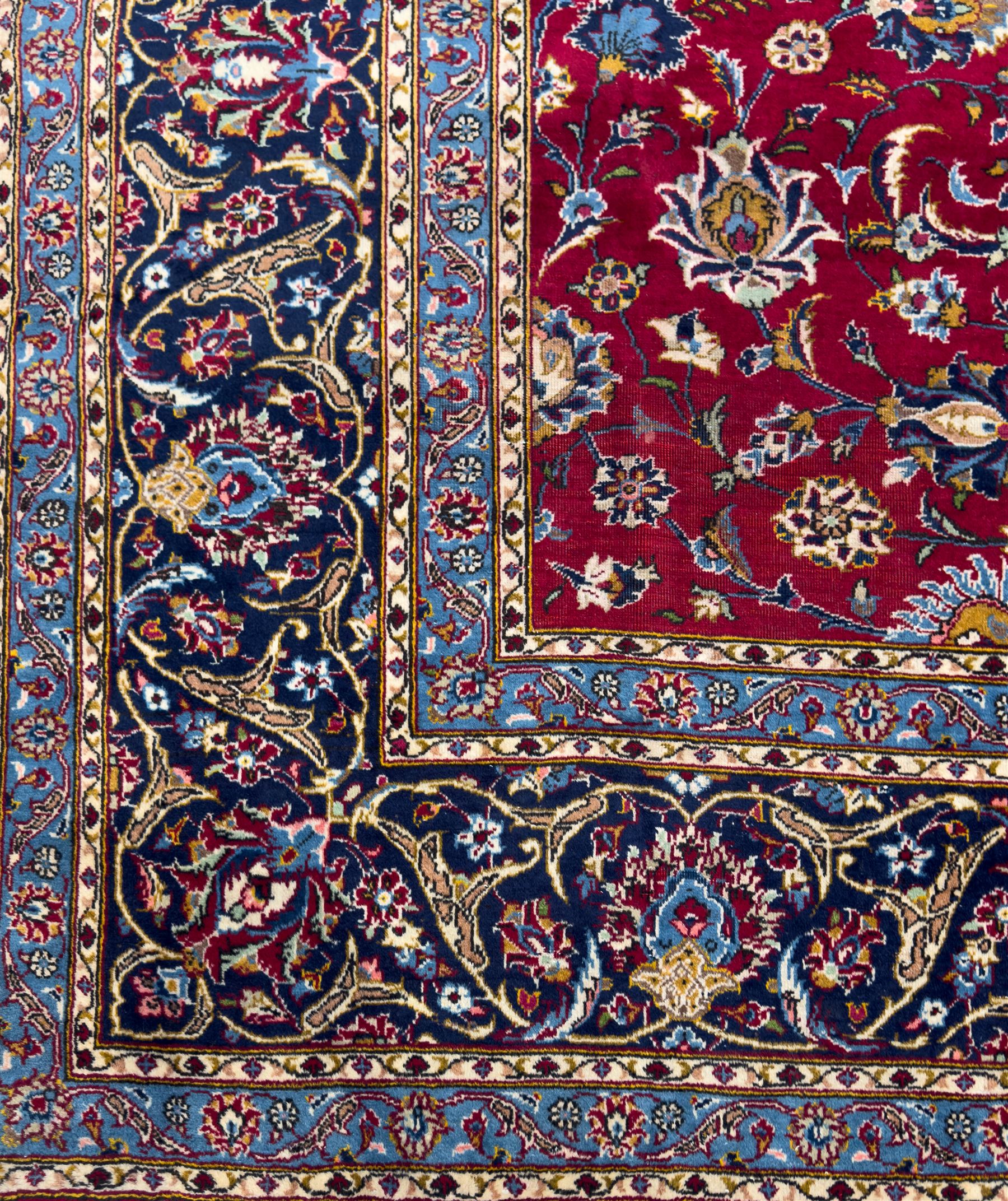 Northeastern Persian Meshed hand-knotted carpet, madder red field with an all-over design of scrolling vines, palmettes, and rosettes, within a dark blue border of palmettes and arabesques 