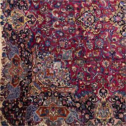 Large North East Persian Meshed hand-knotted carpet with signature, raspberry red field with central shaped cusped medallion, densely decorated with intricate arrangement of scrolling vines, and florals designs within conforming spandrels and a dark ground border richly ornamented with stylized flowers, vase and bird ornamentation, enclosed by guard stripes, with cotton fringe ends