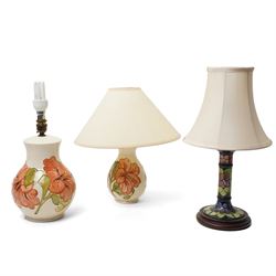 Three Moorcroft lamps in the Violet and Hibiscus patterns, two with shades, largest includ...