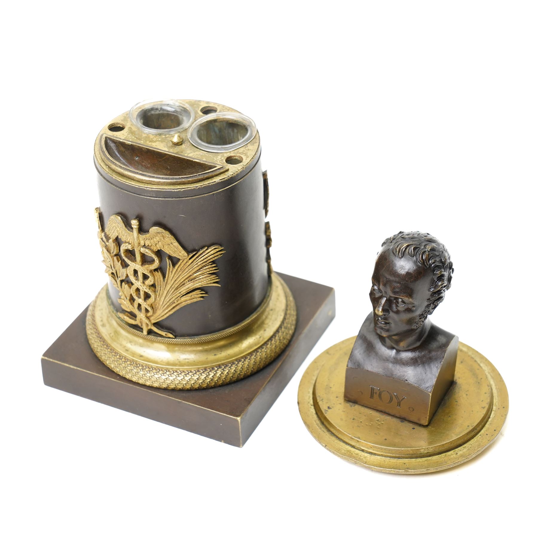 French 19th-century bronze inkwell surmounted by a bust of General Maximilien-Sébastien Foy, the cylindrical column applied with gilt-metal martial trophies and a classical caduceus of Hermes, emblematic of eloquence, commerce and diplomacy, raised on a brass socle cast with a scale pattern, on a square bronze base, the interior fitted with two glass inkwells and bronze pounce pot, H19cm