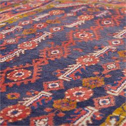 North West Persian Cirjan hand-knotted rug, indigo field decorated with vertical columns of stylized boteh, rosettes and diamond devices arranged in a repeating lattice and a chain of linked lozenges, enclosed by a mustard gold inner border and a principal border of madder ground, flanked by narrow guard stripes, with cotton fringe ends 