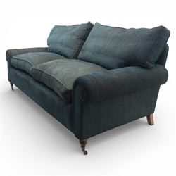 Late 20th century three seat sofa upholstered in green fabric, with gently rounded scroll arms, loose seat and back cushions, raised on turned wooden legs with castors, rear splayed legs