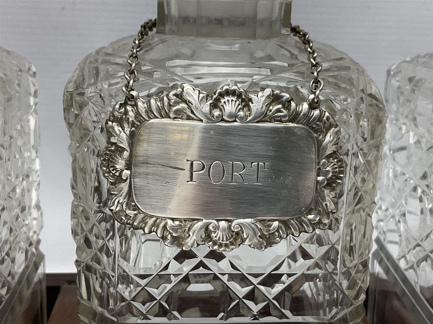Edwardian oak three bottle tantalus, with brass mounts and three square sided cut glass decanters each with hallmarked silver decanter labels, complete with key, H31cm