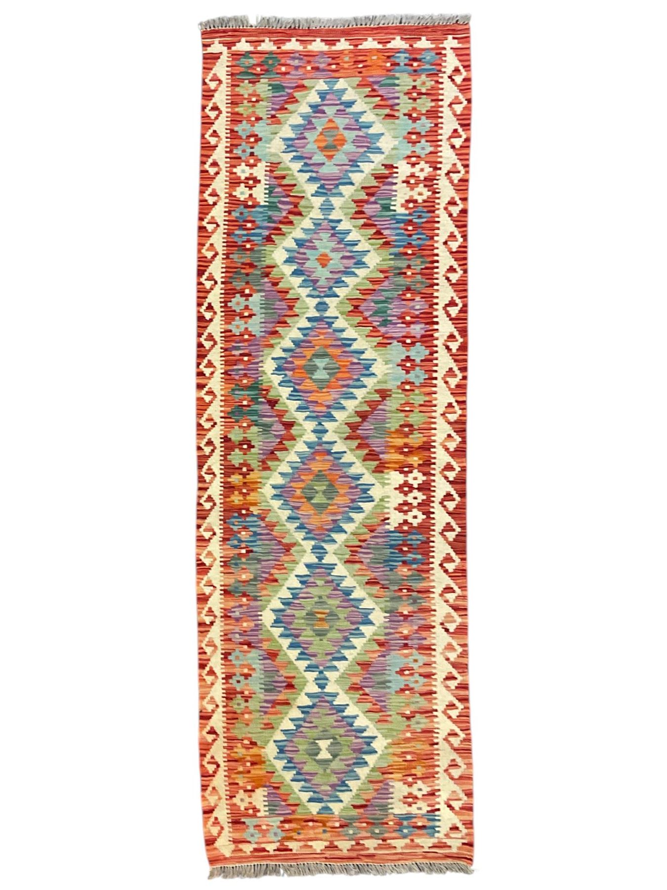 Chobi Kilim red ground and multi-coloured runner, decorated with overall geometric design, trailing lozenges within hooked border