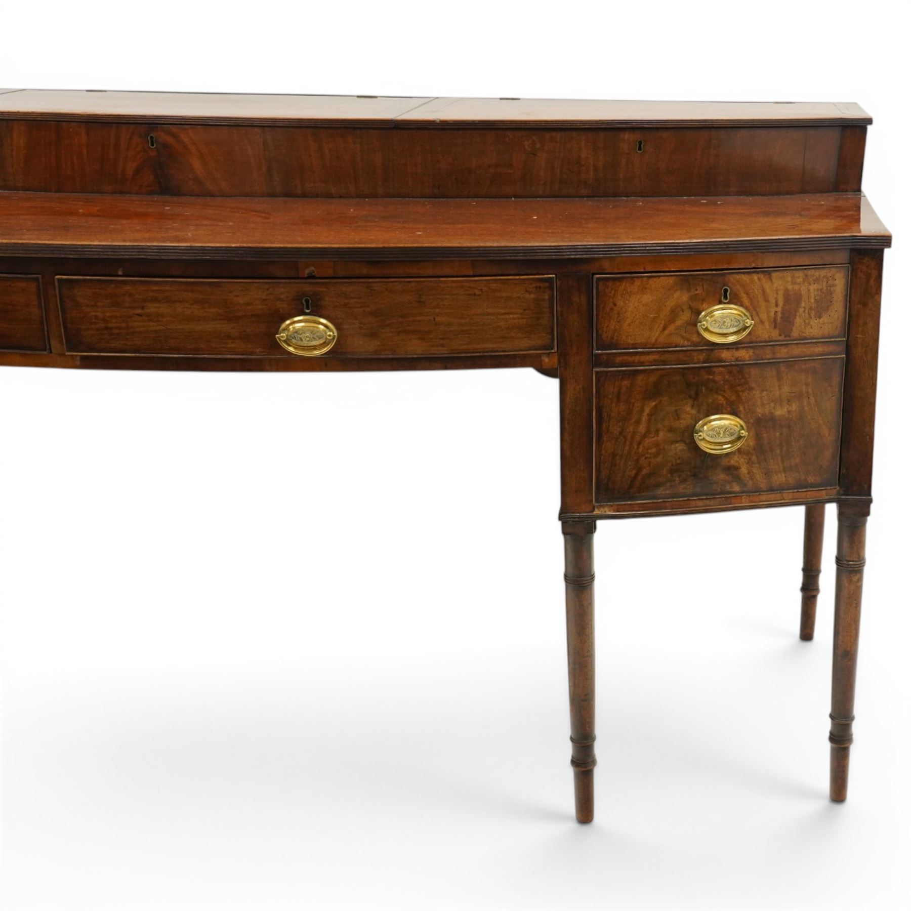 Large George III mahogany bowfront sideboard, the shaped top with raised superstructure fitted with three compartments with hinged tops and reeded edge, the body fitted with two central cock-beaded frieze drawers, flanked by a cellarette drawer and hinged cupboard both with faux double drawer facias, raised on ring turned tapering supports
Provenance: Kirkham Hall