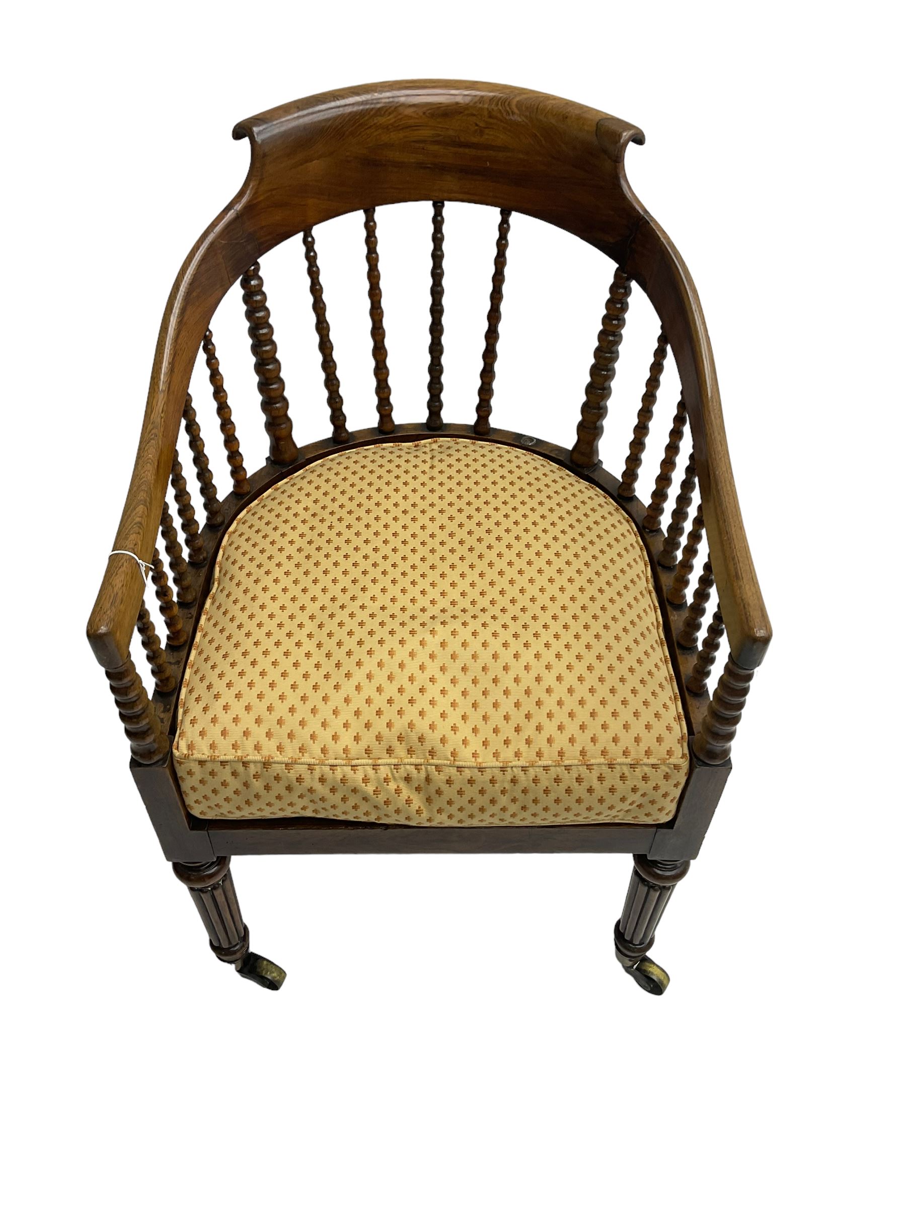 William IV rosewood tub armchair, the arched bow cresting rail over graduated bobbin turned spindles, cane seat with loose cushion, terminating in brass cups and castors.