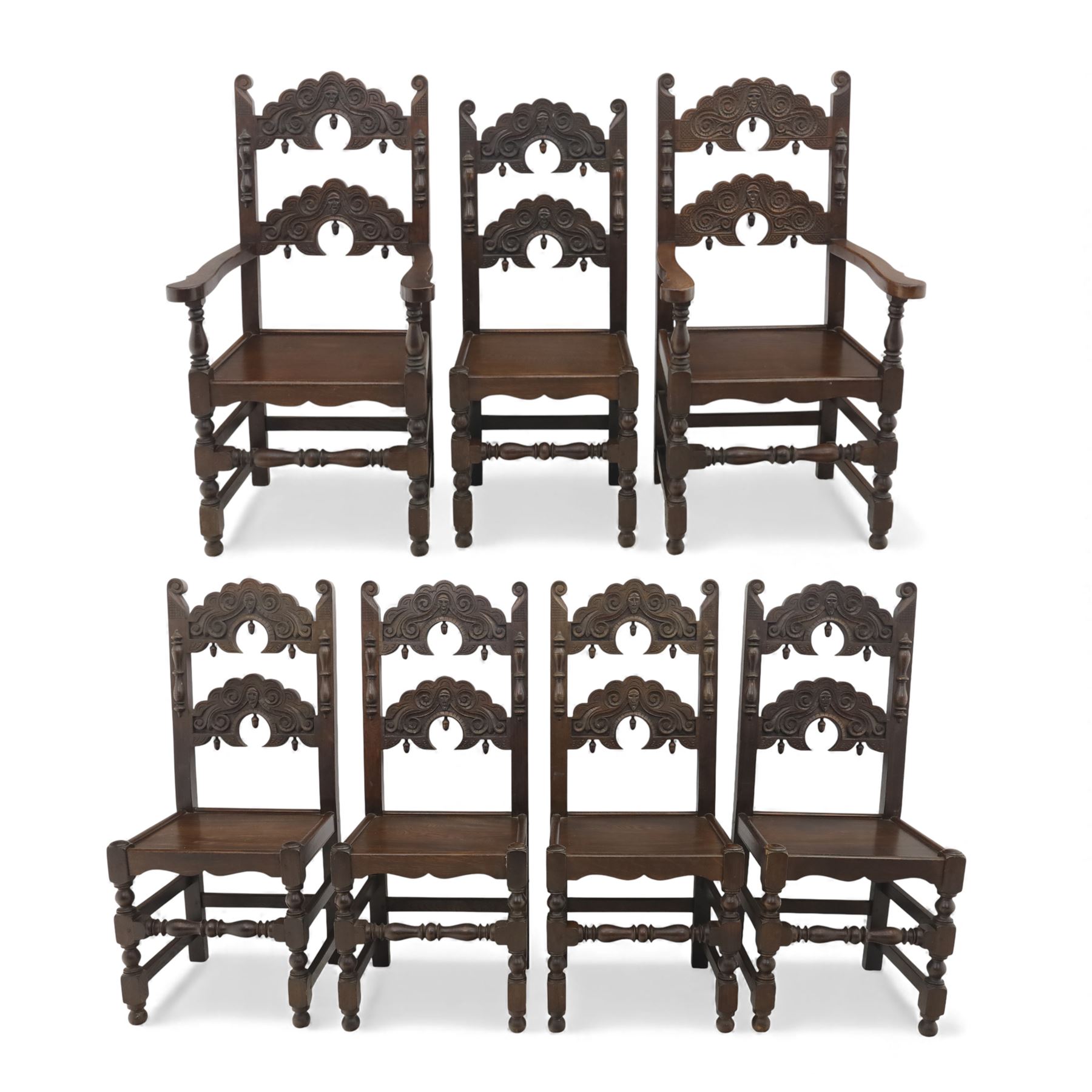 Early 20th century set of seven Jacobean Revival oak chairs, comprising pair of cavers and five chairs, each with carved mask and scroll decoration to the crest and and back rail, plain oak seat, upon turned front legs and block rear legs with conforming stretchers
