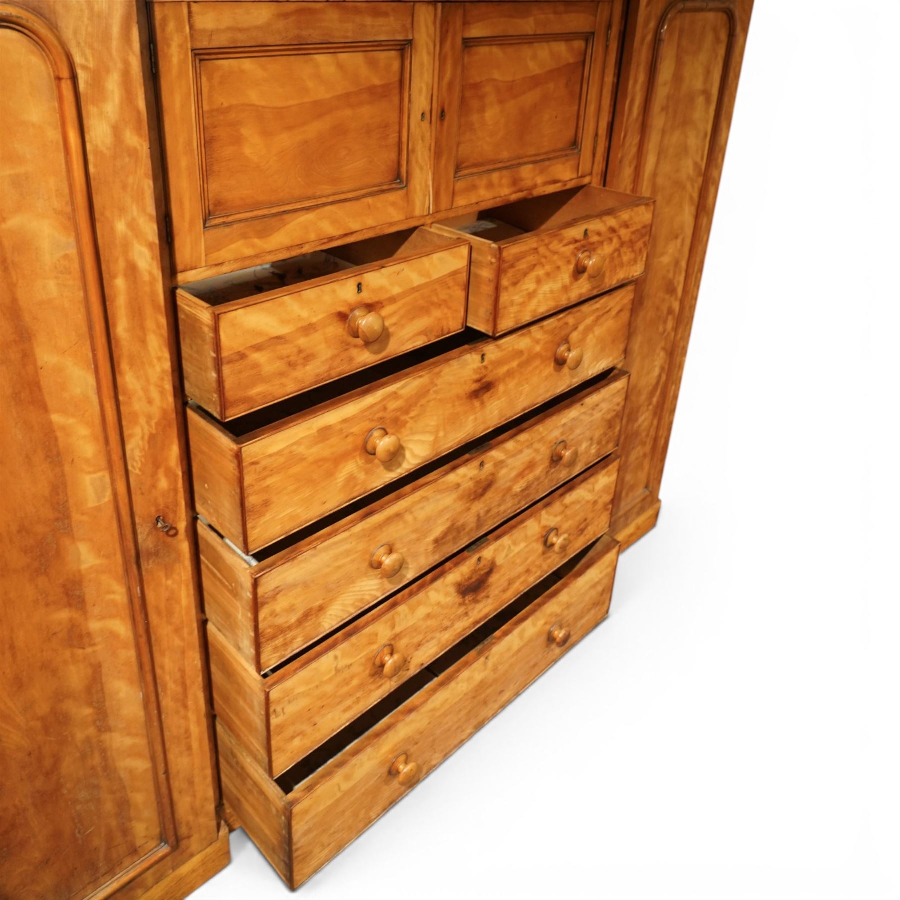 Victorian satinwood reverse breakfront triple wardrobe, projecting moulded cornice over twin full-length panelled cupboard doors flanking central linen press section, fitted with two cupboard doors above two short and four long drawers, turned wooden handles and moulded plinth base