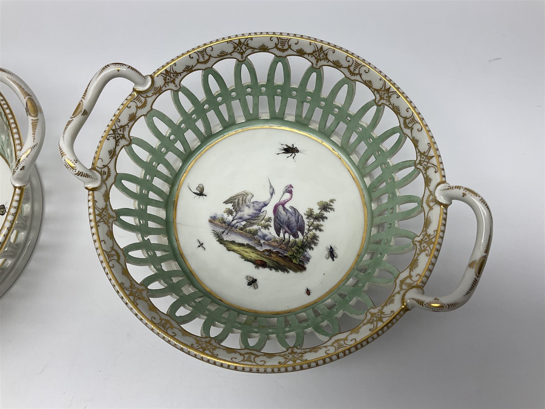 Pair of 19th century German openwork chestnut baskets, with twin handles and scrolling gilt border and star rim, painted to the centre with birds and insects, D22cm 