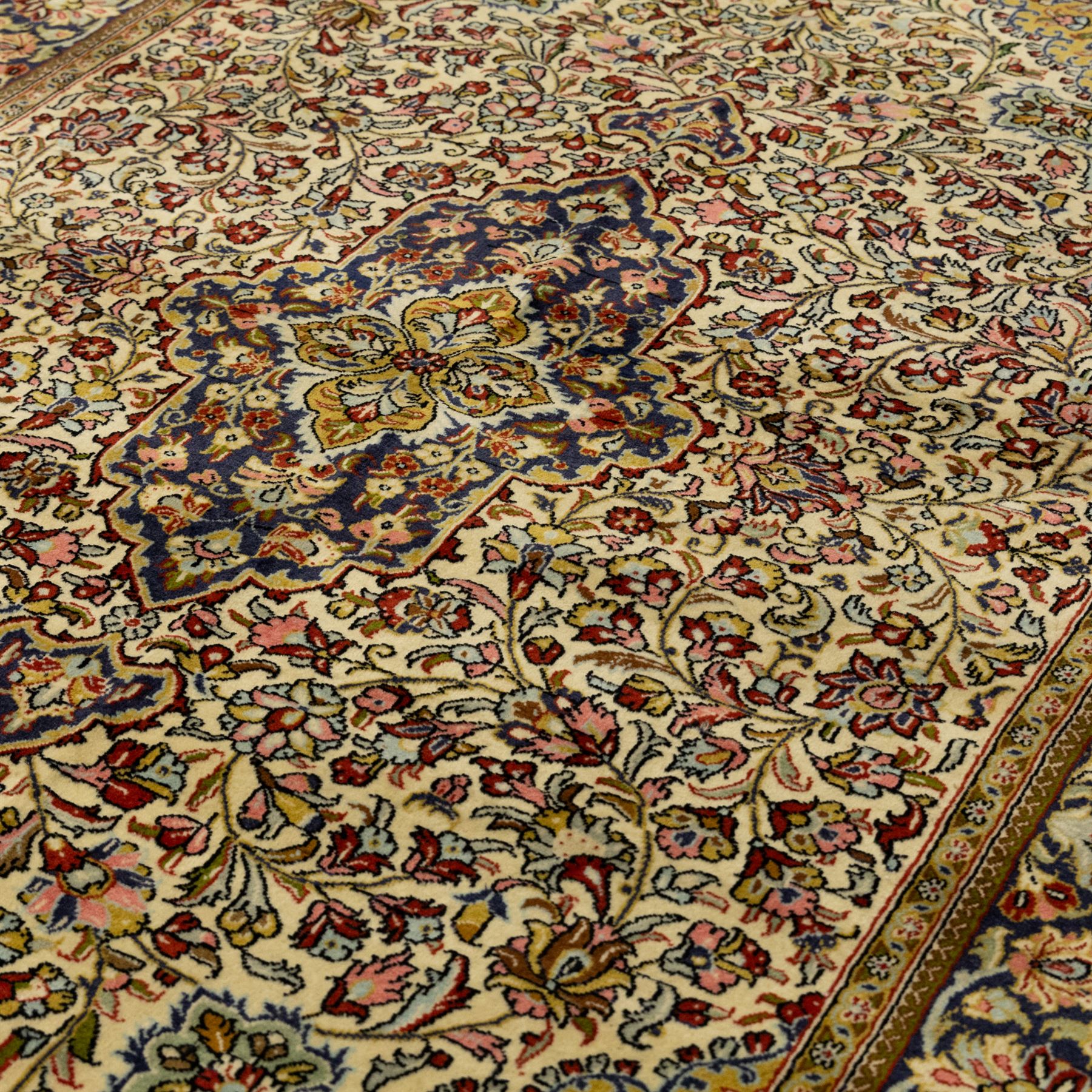 Fine Qom hand-knotted rug, ivory ground, with a dark navy shaped floral medallion and pendants, the field densely worked with fine flowering vines, palmettes and leafy scrolls in red, green, ochre and blue tones, within golden spandrels and a dark navy floral border, flanked by narrow guard stripes, with cotton fringes