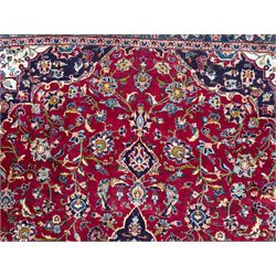 Pair of Persian wool rugs, each with rich red ground, one centred with a diamond-shaped medallion and navy spandrels within a floral field, the other with radiating floral medallion and scrolling foliate motifs, both enclosed by multiple borders with palmette and flowerhead designs, from the region of Kashan 291x376, 299 x 378 