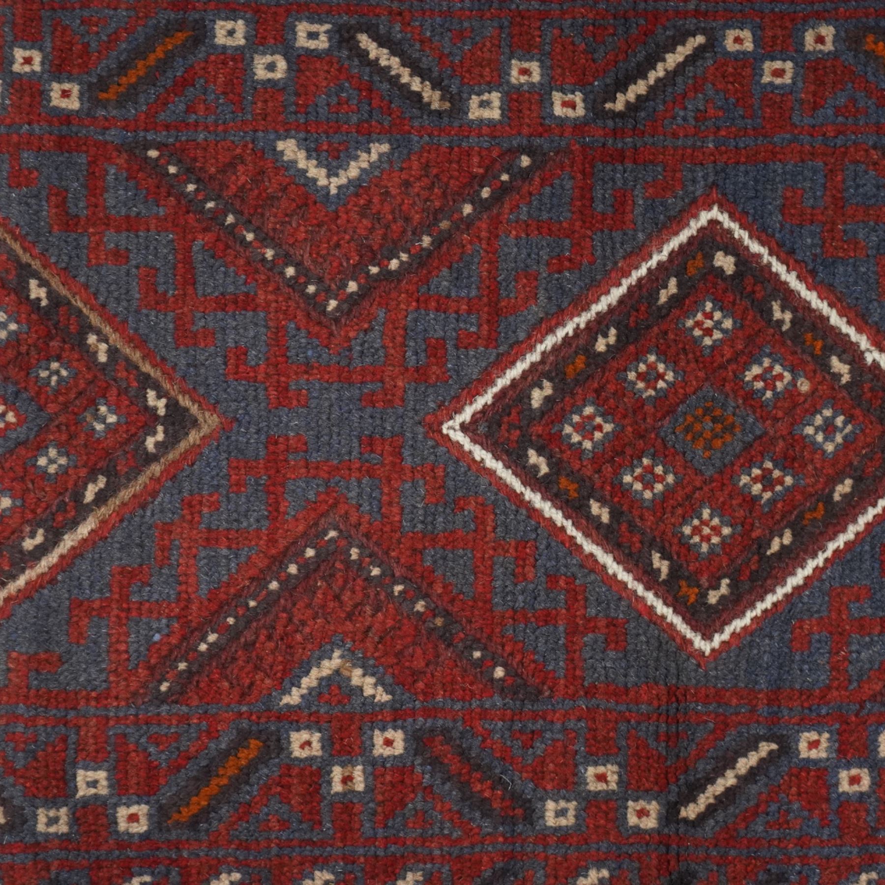 Afghan hand-knotted wool runner, dark red and indigo blue madder, with a repeating diamond medallion design within multiple geometric borders, with flatweave ends 
