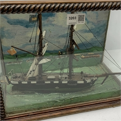 Victorian scratch built water-line model of a two-masted sailing ship with wooden hull and furled sails L31cm in glazed display case with rope twist mounts, the backboard painted with a coastal harbour scene L37cm H29cm D22cm
