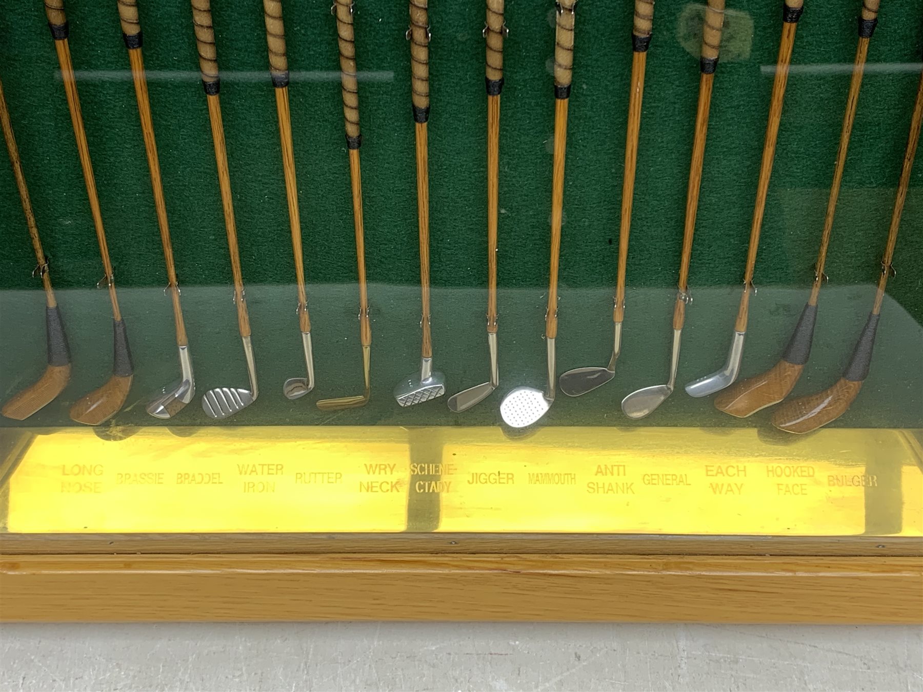 Modern handcrafted miniature set of fourteen 19th century style golf clubs by P.D. Rushworth dated 2000, each with turned wooden shaft and leather grip, comprising four woods including long nose driver, brassie and hooked face, and ten other metal head clubs including jigger, water iron, rut iron, anti-shank iron, wryneck iron, mammoth iron, Schenectady putter, etc., displayed in a baise lined architectural style oak case with hinged door, annotated brass strip and maker's plaque, longest club 28cm, case W52cm, H44cm