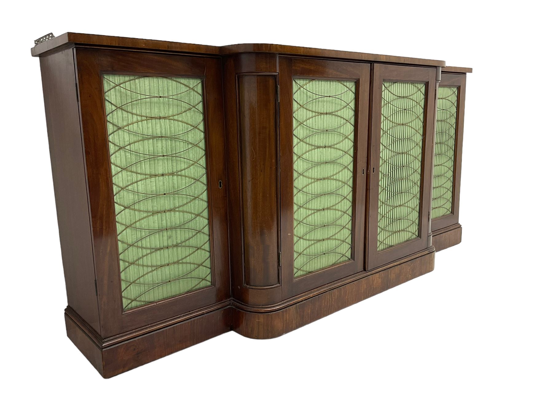 19th century mahogany break-front sideboard, raised brass gallery back with Greek key design, fitted with four cupboard doors, their pleated green fabric overlain with gilt metal grilles, lower moulded edge over plinth base
