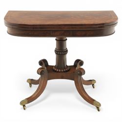 Early 19th century Regency mahogany fold over card table, the rounded rectangular top with brass line inlay enclosing green baize playing surface, crossbanded and strung exterior, with reeded edge above a gadrooned frieze, raised upon a turned column and four reeded sabre supports terminating in brass caps and castors