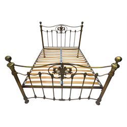 Victorian design king size brass bed frame, featuring an arched headboard and footboard with intricate cast floral and scrollwork centre motifs, flanked by cylindrical supports with ball finials and decorative collars, raised on rounded feet, with a slatted wooden base