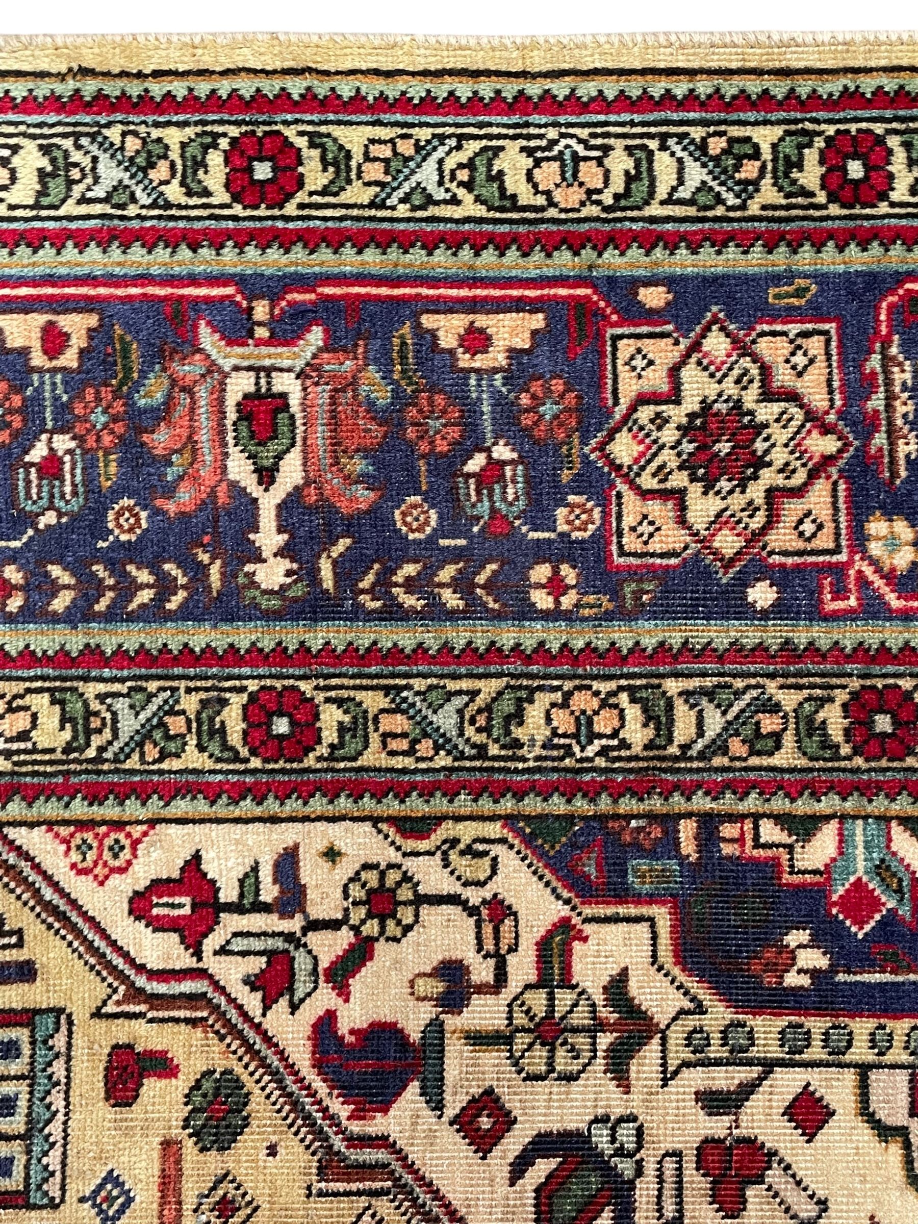 Persian Heriz pale wheat ground rug, indigo pole medallion surrounded by neatly arranged Hac and stylised flower head motifs, indigo main border decorated with alternating palmette motifs, within floral pattern guard stripes 
