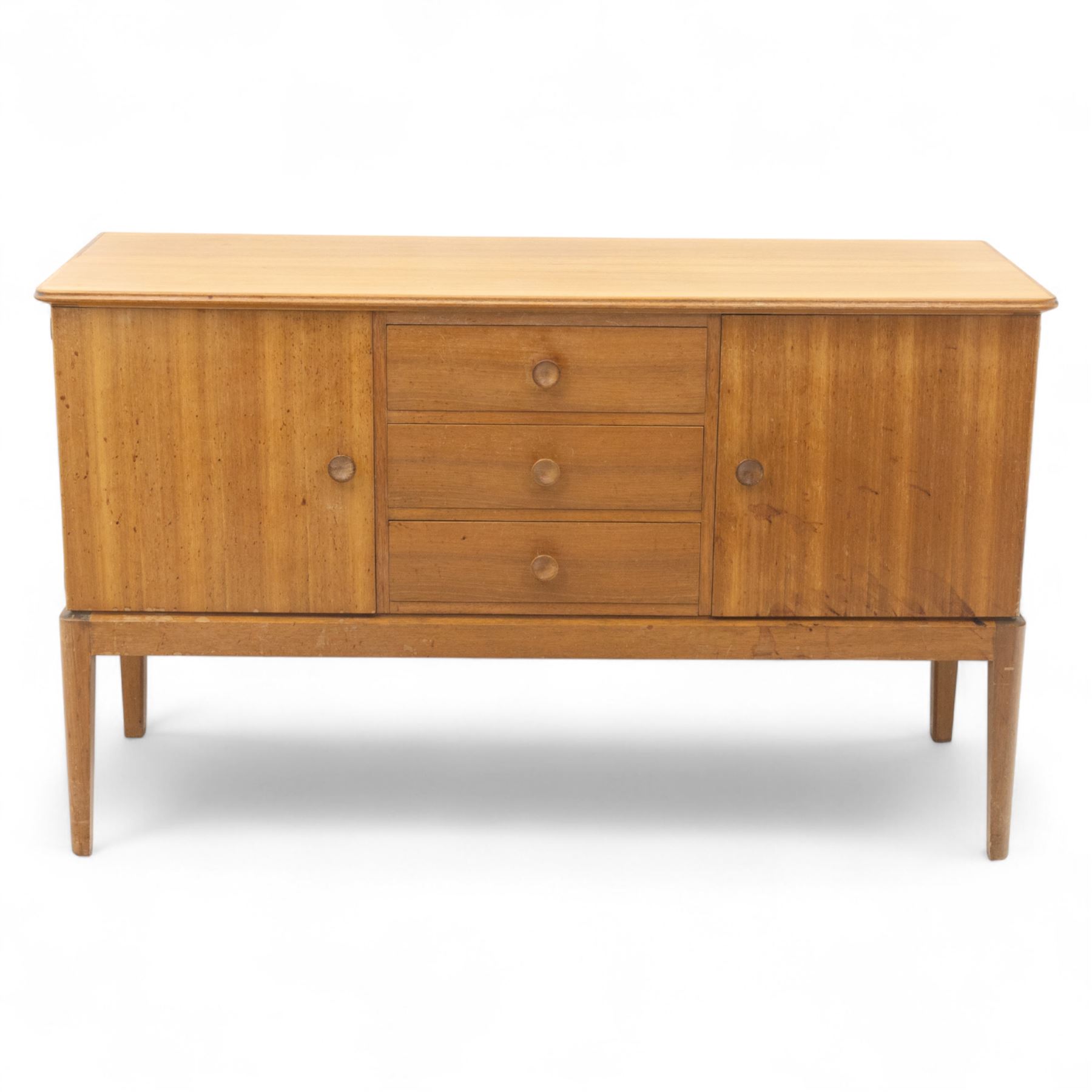 Gordon Russell - mid century modern teak sideboard, the rectangular top with rounded edges over twin cupboards and three central drawers, fitted with circular wooden pulls, on tapered supports, reflecting the firm’s commitment to simplicity and quality materials during the post-war design period