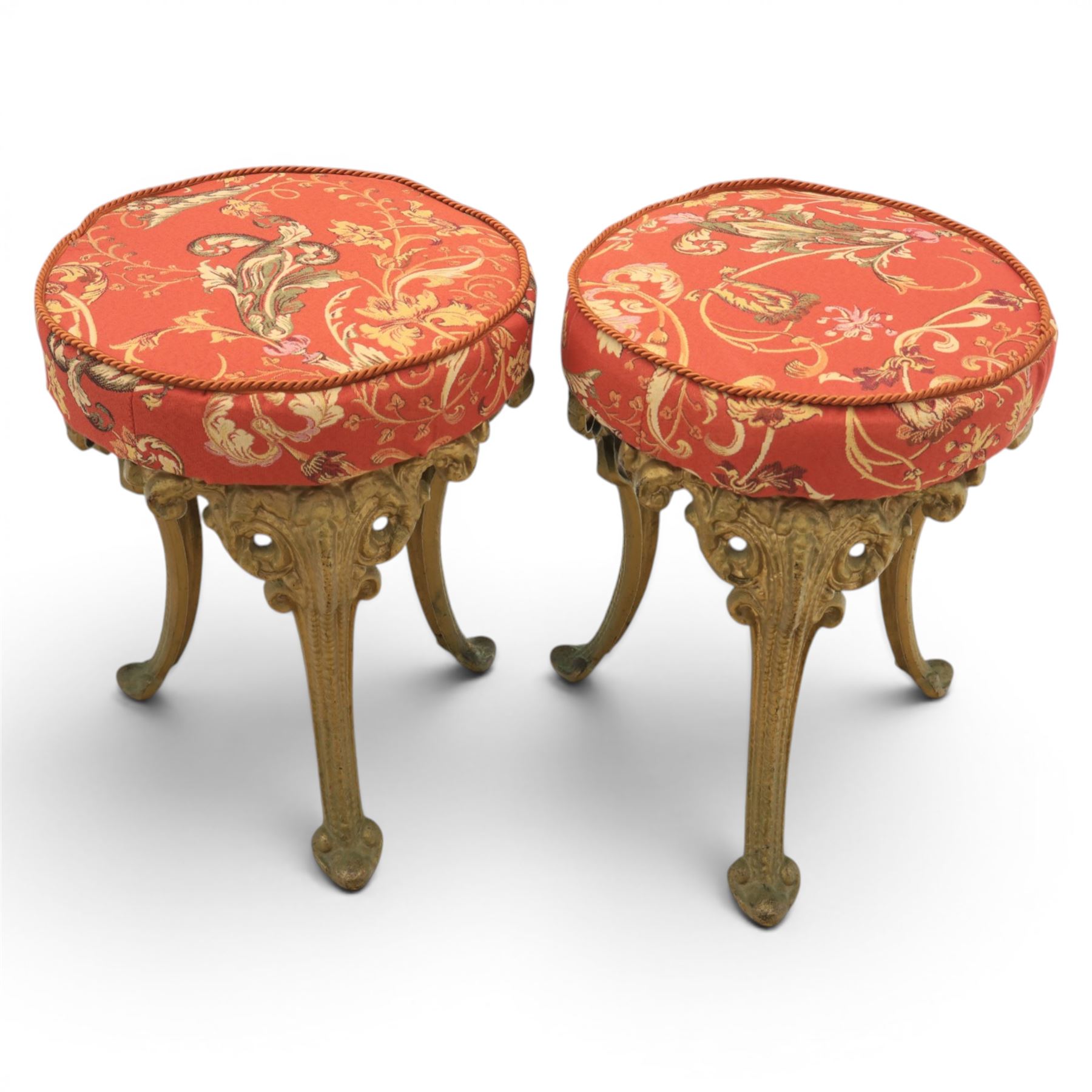 Britannia style cast iron pub table and pair of stools, moulded circular top raised on a gilt painted frame, featuring masks and acanthus detailing united by an under tier, the stools with red floral design (Stools diameter 34cm, height 47cm) 
