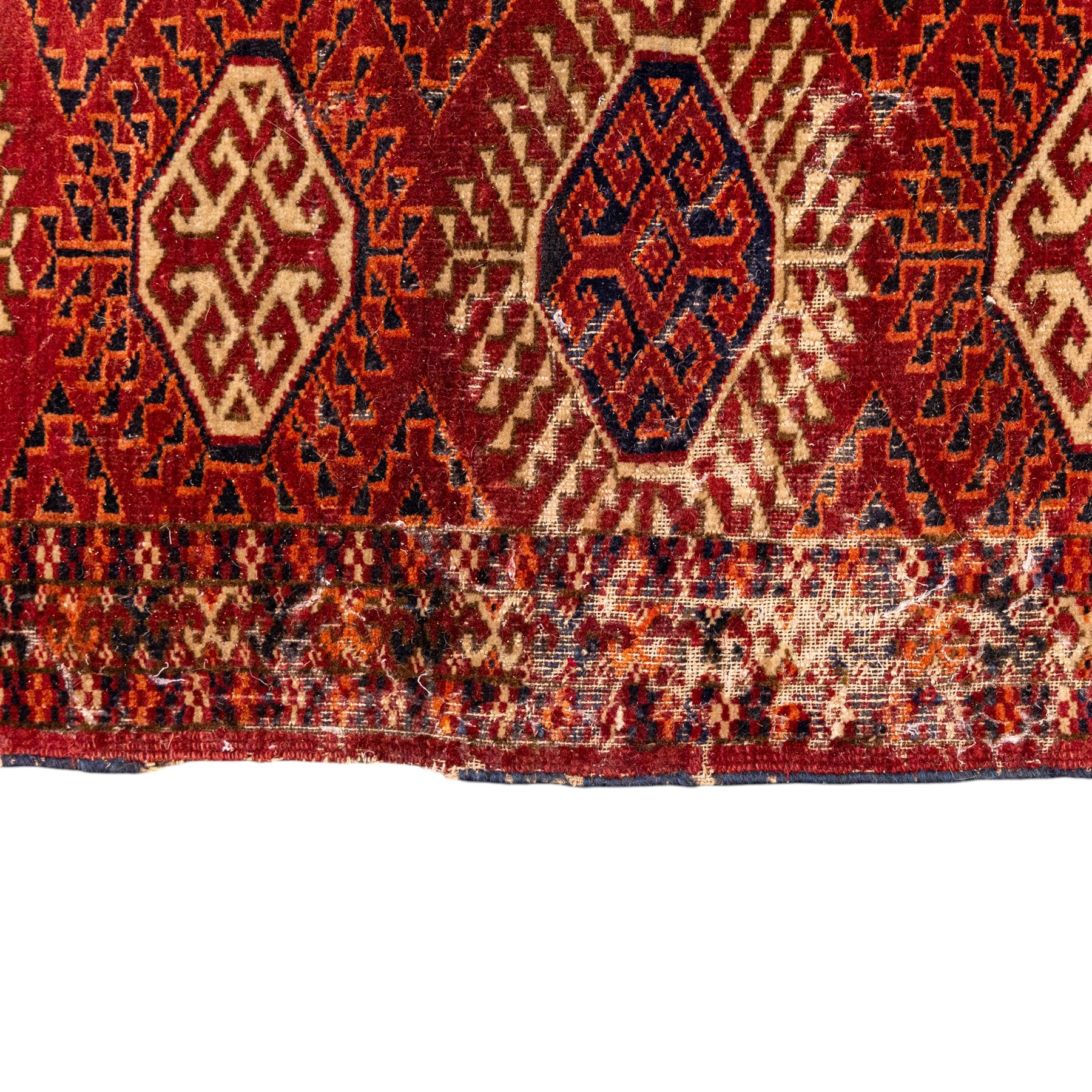 Vintage Bokhara hand-knotted rug, madder field woven in rows of octagonal Tekke guls arranged in vertical columns, each enclosing angular cruciform devices and tribal motifs, divided by narrow indigo lines, within multiple geometric borders incorporating stepped lozenges and latch hook devices, with cotton fringe ends 