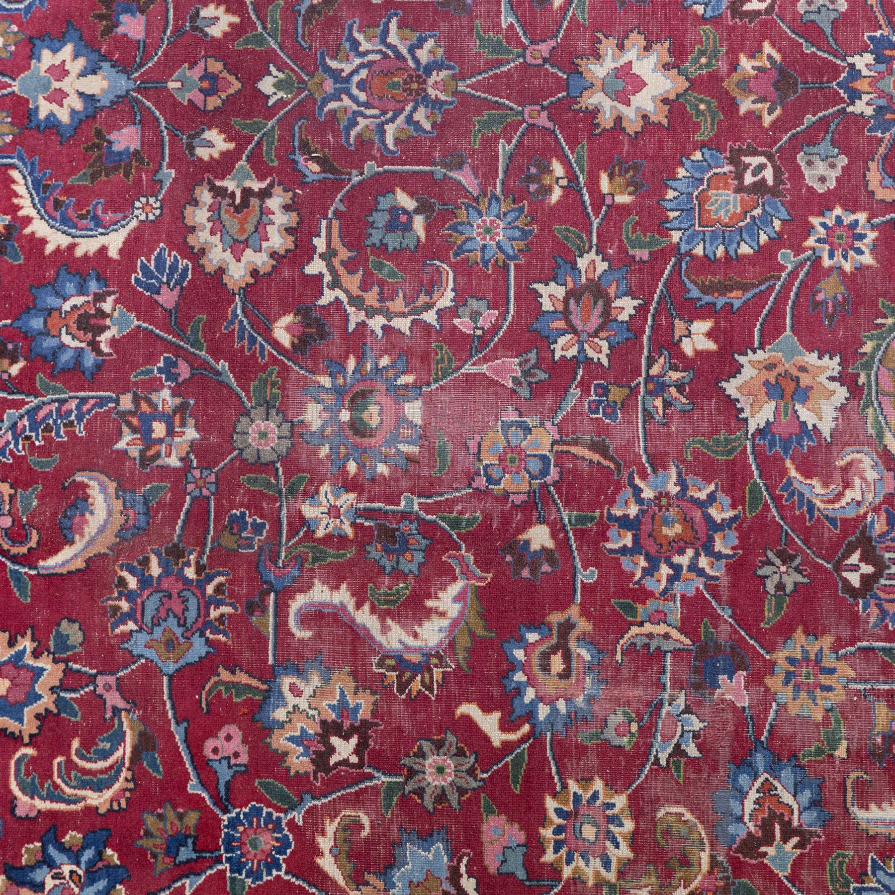 Persian Mashad design wool carpet, the red ground with dense scrolling floral and foliate decoration, within dark blue main border decorated with repeating palmettes and shaped leaves