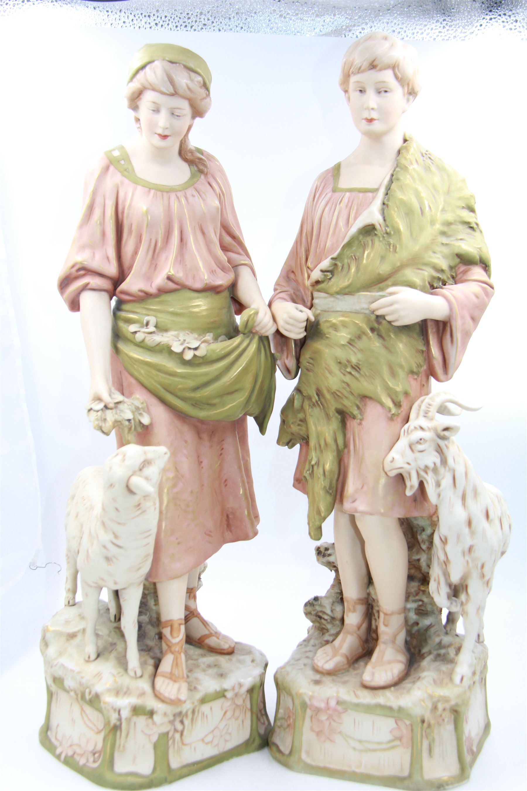 Pair of Royal Dux figures, no. 1115, modelled as a shepherd with a goat by his side and a shepherdess feeding a lamb, each wearing flowing green and pink robes with gilt detailing, with pink triangle mark beneath, H51cm