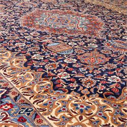 North East Persian Meshed hand-knotted carpet, deep navy field with central complex medallion and densely decorated scrolling floral sprays and palmettes, incorporating cartouche motifs enclosed by a broad tan and dark blue border ornamented by stylized vases flanked by multiple guard stripes, signed 'Amal-e Haji translates as the Work of Haji', with cotton fringe ends 