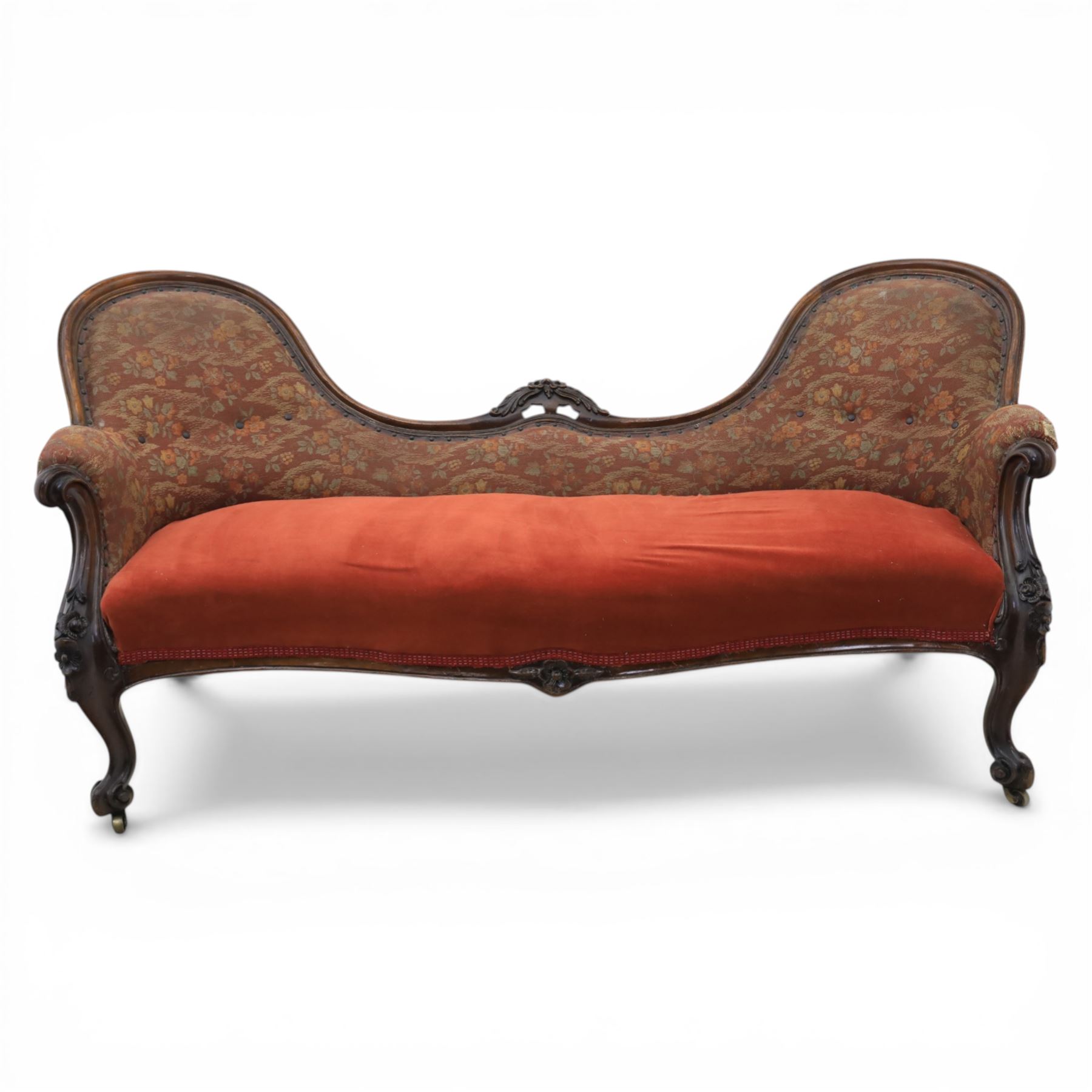 Victorian mahogany framed serpentine sofa, the shaped button upholstered back with central carved foliate cartouche, and scroll arms with carved terminals, over upholstered red seat, upon carved cabriole supports with castors