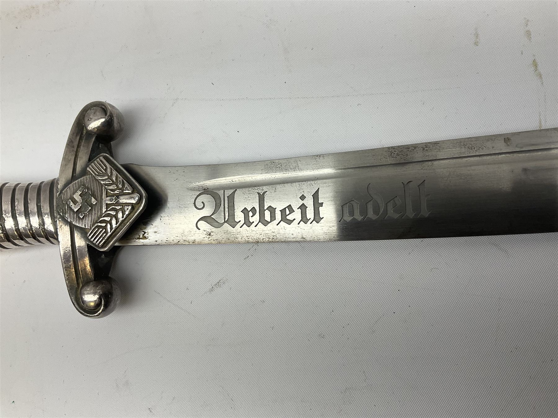 German Reichsarbeitdienst RAD Leader's Hewer dagger, the 26cm single edged scimitar shaped blade with narrow fuller, etched Arbeit adelt; by E.D. Wusthof, Solingen; the aluminium hilt with spade and wheat ear langet; two piece white plastic grip and eagle head pommel; pebbled steel scabbard engraved with ears of wheat and strapwork with double leather hangers L40cm overall