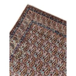 Persian Kirman carpet, the ivory ground field and border decorated with repeating Boteh motifs, interspaced with all-over floral design, blue ground border guards, the top border with signature panel