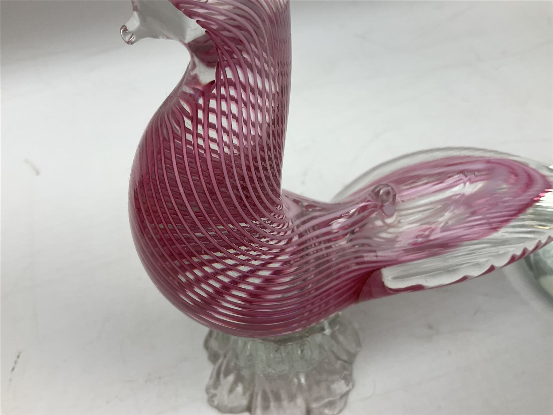 Three Murano style glass cockatoo parrots, the first with mottled yellow, red and orange body, clear outstretched wings, dark blue beak and red crest, raised upon clear stylised base, the second smaller parrot with merging blue and green body, and further with pink striped body, tallest H40cm