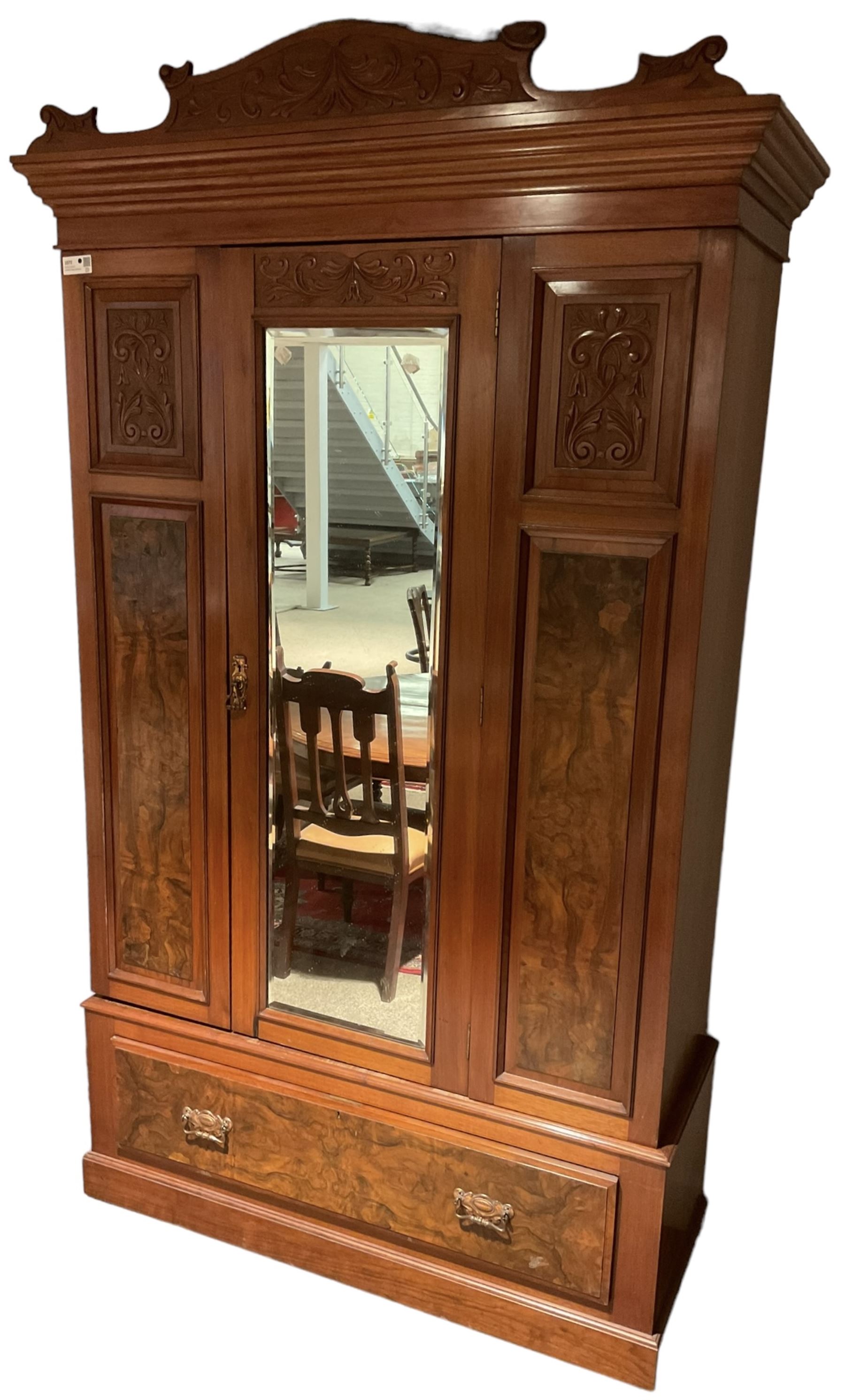 Late Victorian walnut wardrobe, carved arched pediment, fitted with single bevelled mirror door, flanked by carved and figured panels, enclosing hanging rail and hooks, single drawer fitted to base