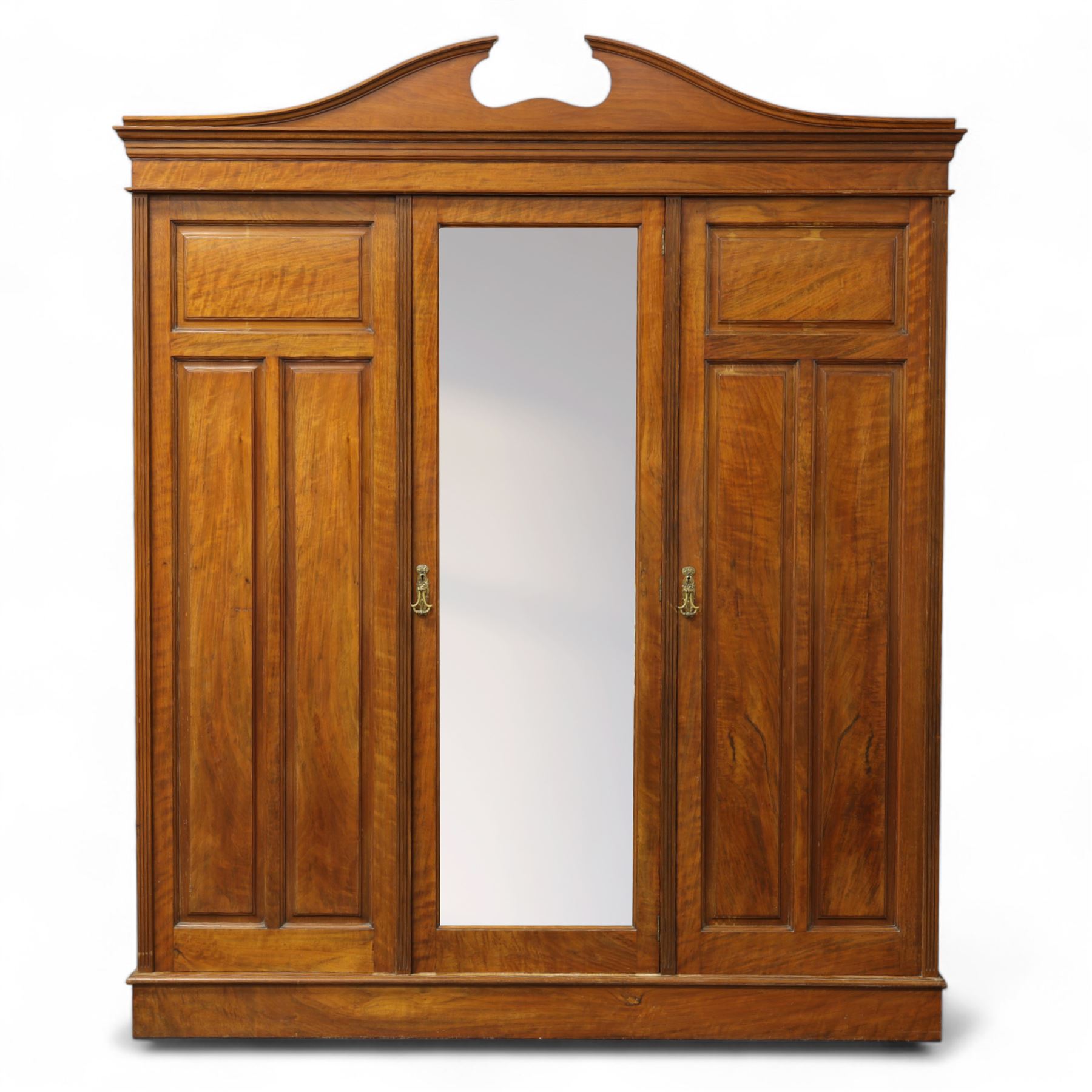 Edwardian walnut triple wardrobe, shaped broken-arch pediment over three doors comprising central mirrored door flanked by moulded raised and fielded panelled doors, interior fitted with hanging space and a bank of three open drawers above three brass recessed-pull drawers, on moulded plinth base