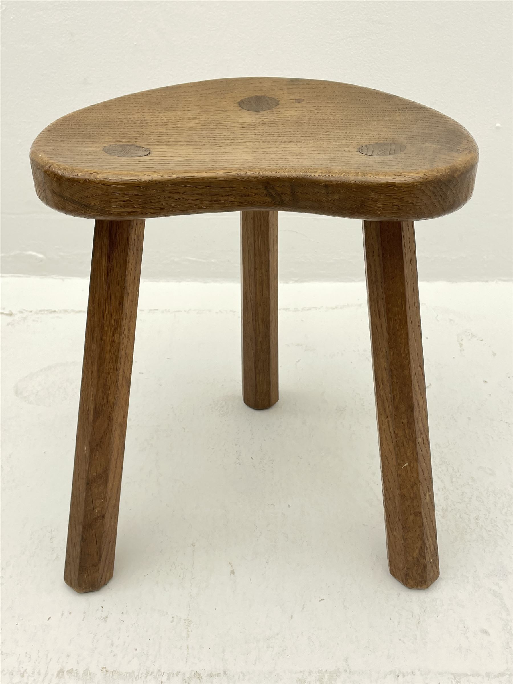 'Mouseman' oak three legged stool with dished kidney shaped seat, tapered octagonal supports, with carved mouse signature, by Robert Thompson of Kilburn 