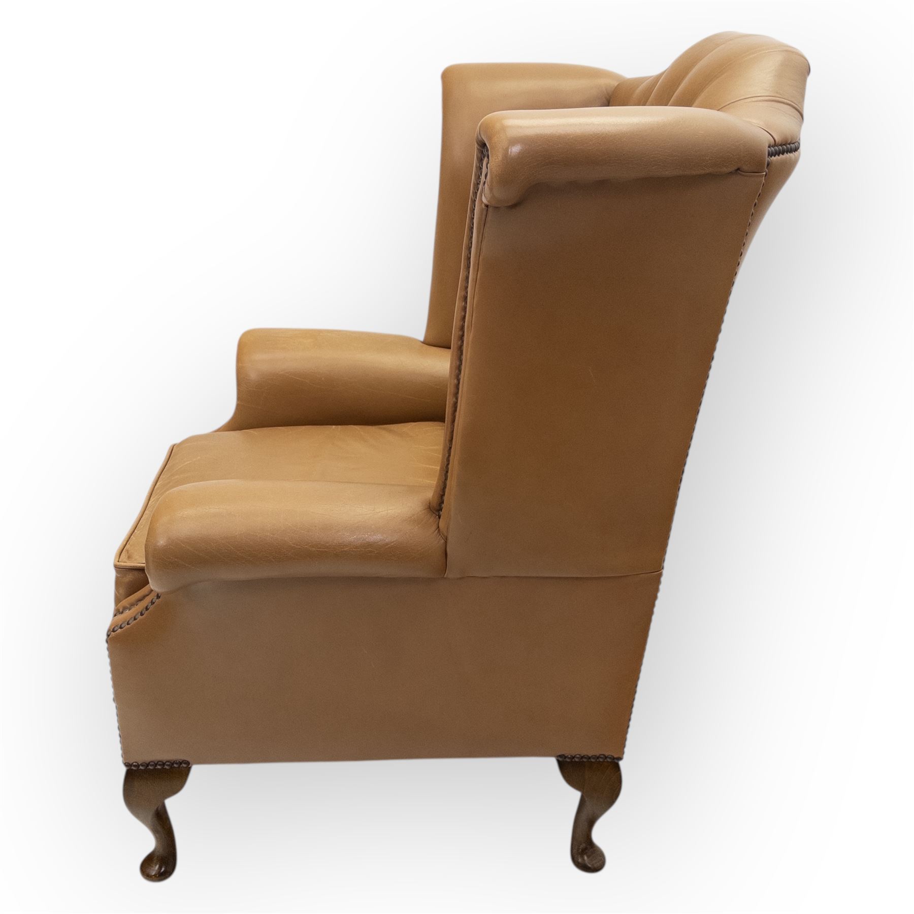 Contemporary set of two tan leather armchairs, comprising a deep-buttoned chesterfield and a matching wingback chair, both with rolled arms, studded borders