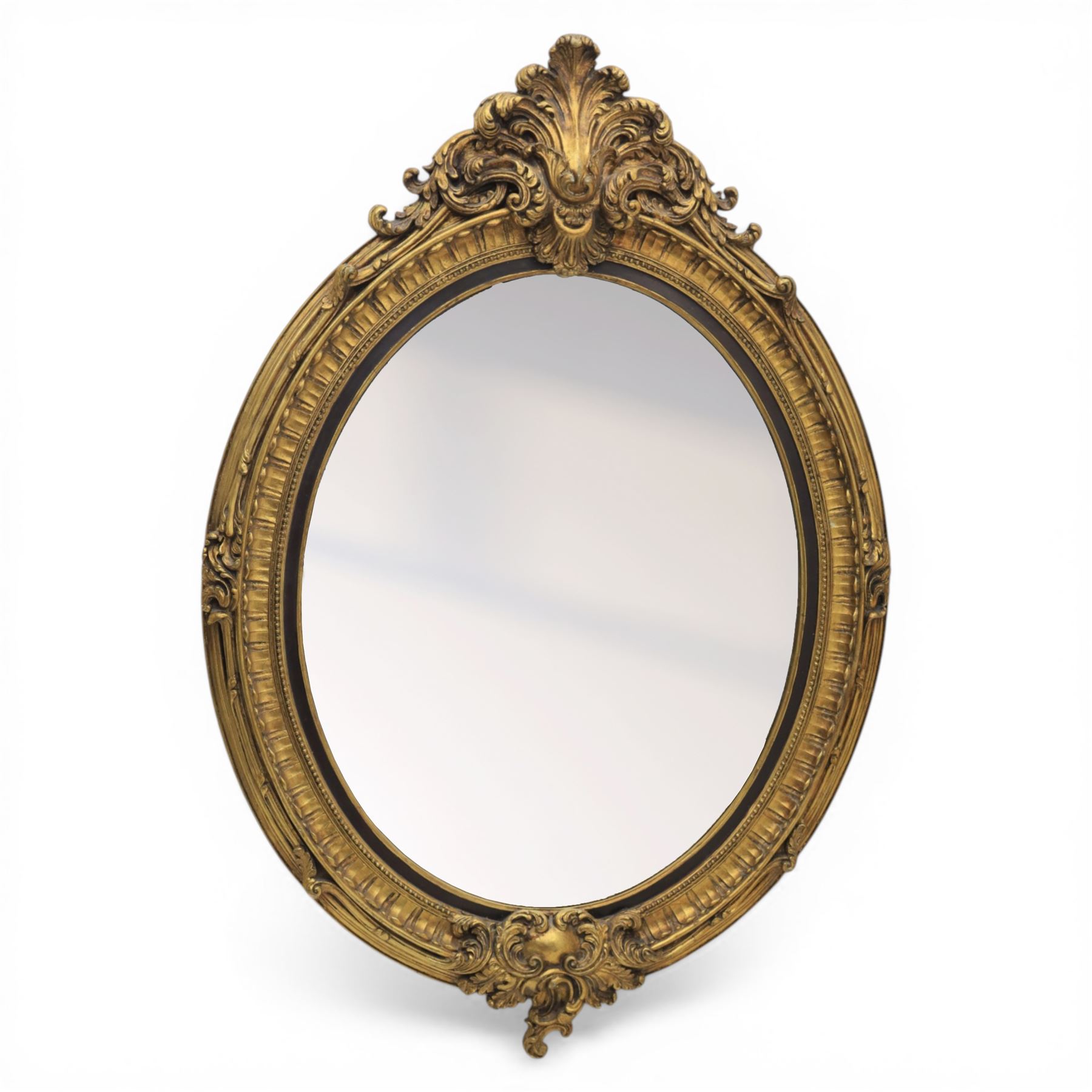 Rococo Revival style gilt composition oval wall mirror, moulded oval frame with fluted and beaded bands enclosing a bevelled mirror plate, the outer frame with acanthus leaf and scroll carved cresting to each side