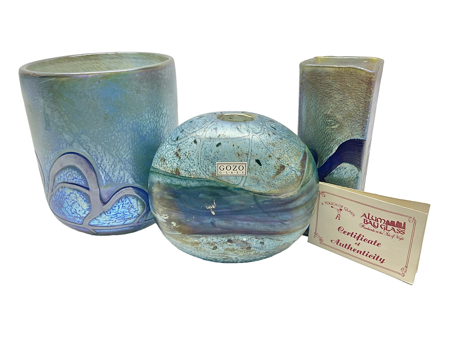 Two Isle of White glass vases, by Alum Bay Glass, both with blue swirl design upon an iridescent mottled blue/green ground, together with a Gozo Glass vase of pebble form, with similar design, H12cm