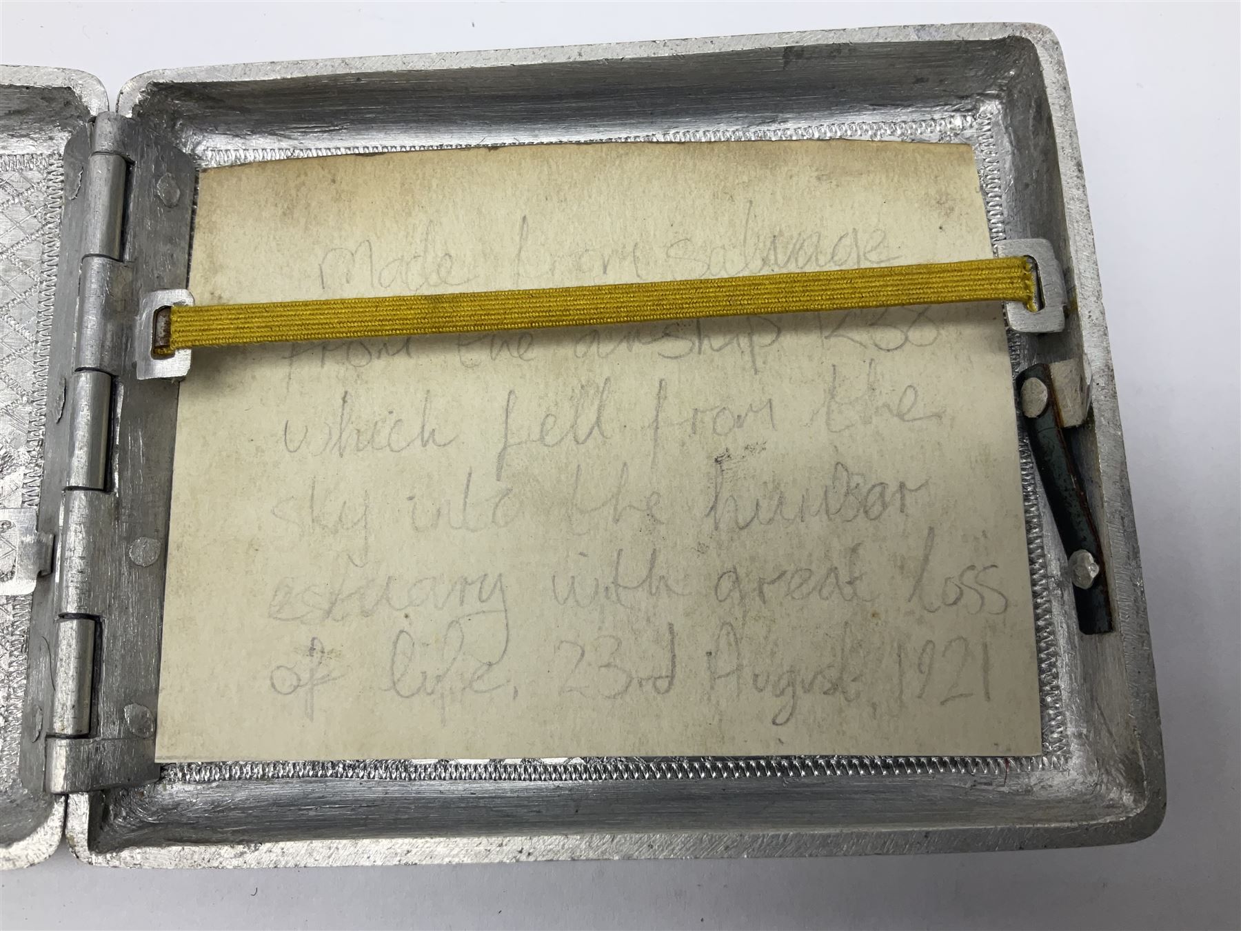 Aluminium cigarette case, by repute made from the R.38. Airship wrecked over Hull August 24th 1921, together with a aluminium matchbox cover, the front inscribed 'R38 WRECKED AT HULL 24 AUG 1921 44 LIVES LOST', the event illustrated verso, (2)