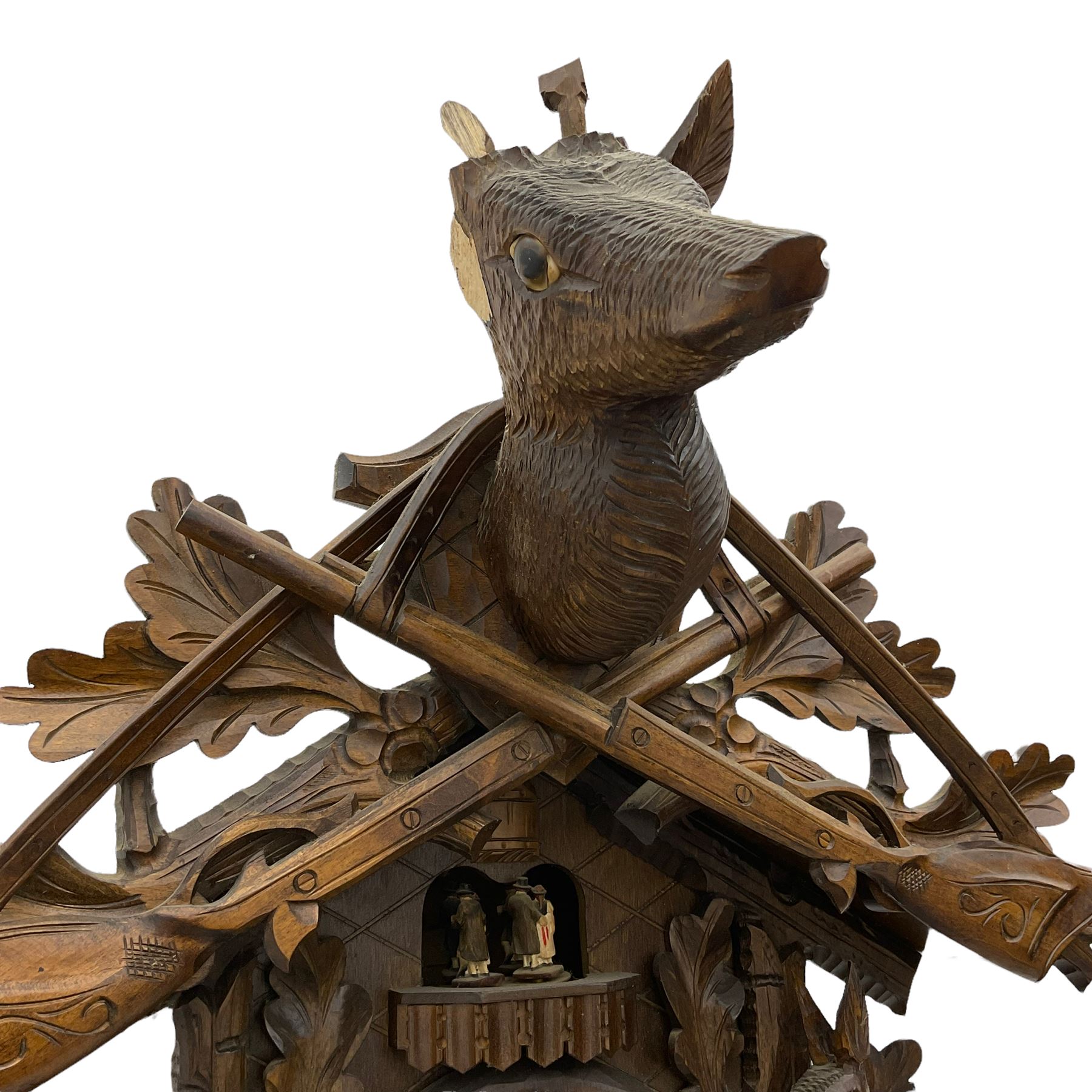 A large and imposing 20th century three train 30hr cuckoo clock with automata and musical features, profusely carved case with a carousel, animals, leaves and sporting guns, dial with pierced wooden numerals and wooden hands, with three weights and pendulum, strike/silent facility. 

