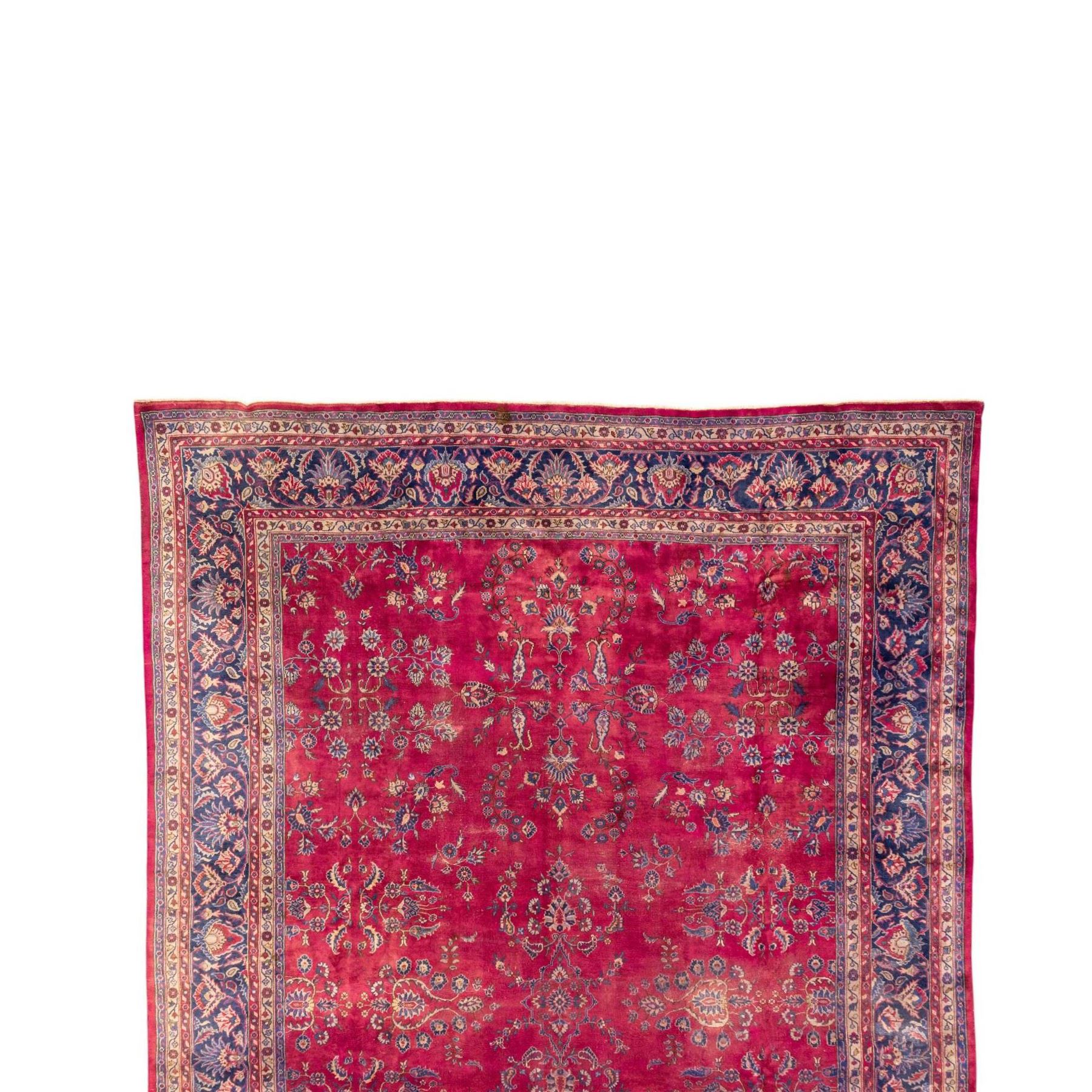 Large Persian-style mahal-type hand-knotted carpet, of rectangular form with a deep crimson field decorated with an all-over arrangement of stylized floral sprays and palmettes, with a central subtle medallion composition enclosed by a dark navy main border of scrolling floral motifs between narrow guard stripes with fringe ends 