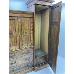 Late 19th/early 20th century oak drop centre wardrobe, central cupboard over three drawers flanked by two taller compartments with hanging space enclosed by panelled doors, each with projecting cornices and fluted friezes, the doors carved with square leaf motifs, reverse break front plinth base