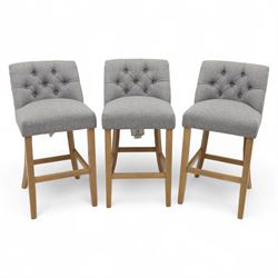 Contemporary set of three upholstered bar stools, each with button-tufted grey fabric back...